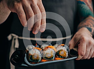 Man sprinkles spices on sushi rolls to serve the dish.