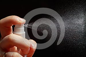 Man sprinkles a spray of perfume or sanitizer on a black background. Water spray or insecticide against insects or pests