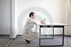 Man squatting at the desk, working with tablet