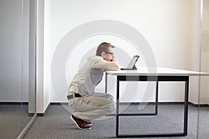 Man squatting at the desk, working with tablet