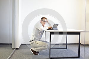 Man squatting at the desk, working with tablet