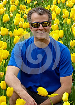 A man squatting down in front of a yellow tulips gardrn