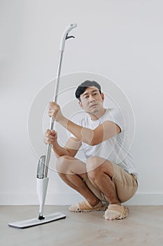 A man is squatting down while holding a mop