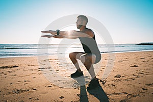 Man squatting or exercising on the beach during sunset. Sports and health