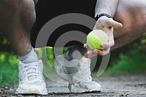 man squatting holds a tennis ball in his hand