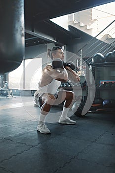 Man Squatting With Kettlebells At Gym. Asian Sportsman On Intense Workout At Fitness Center.