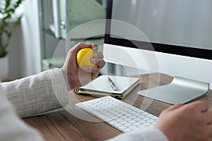 Man squeezing antistress ball while working with computer in office