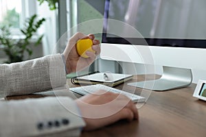 Man squeezing antistress ball while working with computer in office, closeup