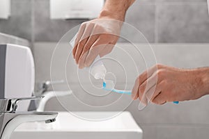 Man squeezing toothpaste from tube onto toothbrush in bathroom, closeup