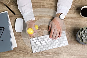 Man squeezing yellow stress ball while typing on computer keyboard at table, top view