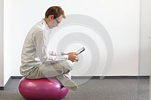 Man on stability ball working with tablet