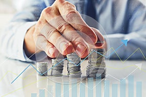 A man stacks coins with a chart of investments