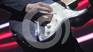 A man on stage plays on a white electric guitar, close-up