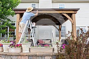 Man staining a backyard gazebo behind his house