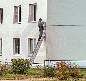 A man on the stairs installs a CCTV camera on the wall of the house