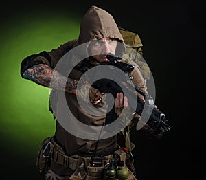 Man Stalker with a gun with an optical sight and a backpack on a dark background