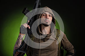 Man Stalker with a gun with an optical sight and a backpack on a dark background