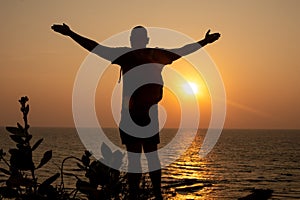 Man stand with arms wide open on beach and look at water. Traveler spend past day close to waves, watch sunset.