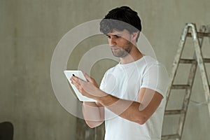 Man stand in new apartment, using tablet, choosing new design of house. Home repair