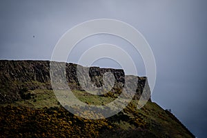 Man standing alone at Salisbury Crags in Edinburgh during a cloudy day, telephoto