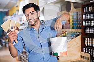 Man standing amongst racks in paint store with brushes and paint