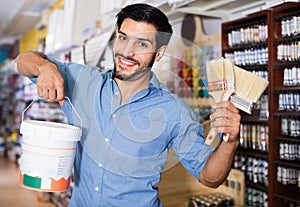 Man standing amongst racks in paint store with brushes and paint