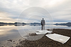 Man standing at the beach, ice floes on dark sand, calm sea, mist and fog. Hamresanden, Kristiansand, Norway