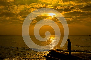 Man standing at the beach looking at bright red storm clouds during sunset.