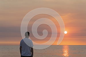 Man standing on beach sand looking towards horizon at orange sunset. Vacation concept.