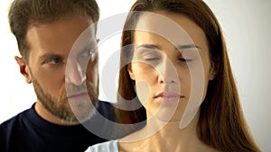 Man standing behind wife, sad lady with closed eyes hearing husband decisions