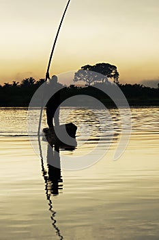 Man standing in a boat at the sunrise on a lake