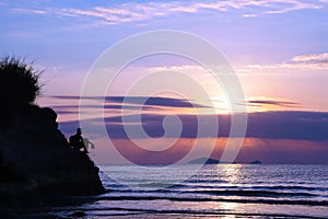 A man standing with a camera on a cliff by the sea at sunrise