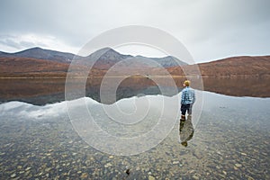 Man standing in clear lake surrounded by the Scottish Highlands