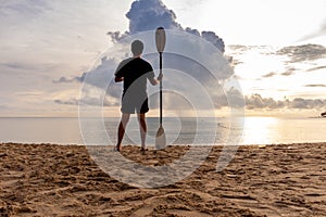 Man standing on clear sand beach and hold Paddle