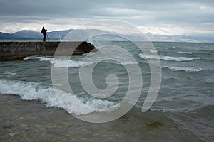 Man standing on concrete pier at wavy sea.