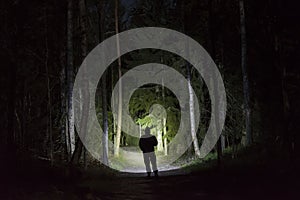 Man standing in dark forest at night with flashlight and hoodie on head