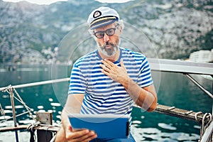 Man standing on the deck of his boat and using digital tablet on a sunny afternoon