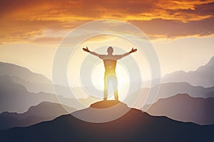 Man standing on edge of mountain feeling victorious with arms up in the air.