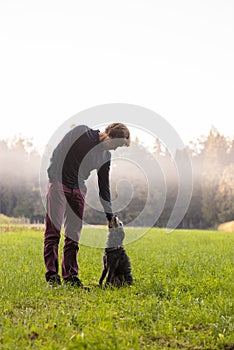 Man standing enjoying nature as he bends down to his dog to pat