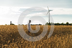 A man standing in a field looking at a wind generator