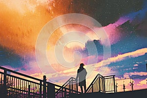 Man standing on footbridge against colorful sky