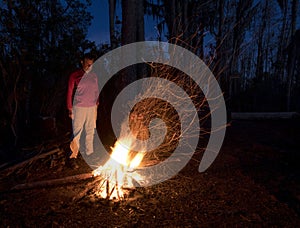 A man standing in front of a campfire at night in the forest