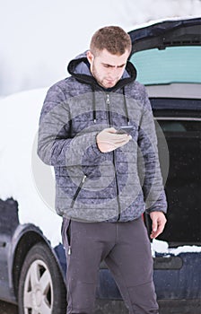 Man standing in front of damaged car and calling car services to