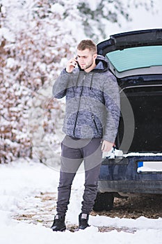 Man standing in front of damaged car and calling car services to