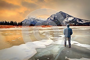 Man standing on frozen Vermilion Lakes in Banff watching golden sunrise over Mount Rundle