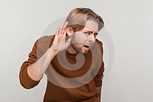 Man standing with hand on ear and want to hear something, listening to interesting talks.