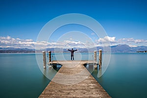 Man standing with hands wide open on a jetty by tranquil lake