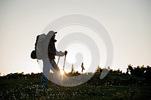 Man standing on the hill field with hiking backpack and sticks