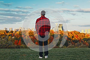 Man standing on hill in front of city urban town dreaming of future or remembering past time. View from back.