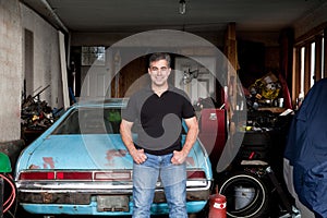 Man standing in his cluttered garage next to an old car.